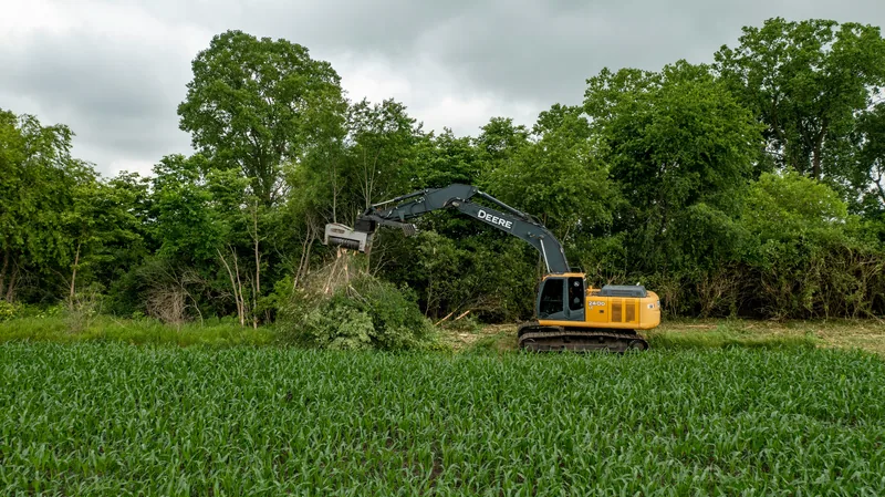 John Deere excavator clearing trees at the edge of an agricultural field in Ontario — heavy equipment used in land clearing explained