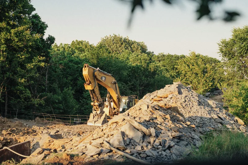 CAT excavator on a rocky cleared construction site with trees in background in Ontario