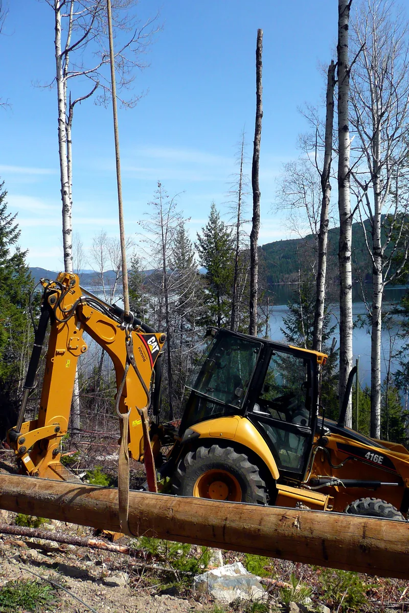 CAT backhoe excavator clearing trees on a lakefront property in Muskoka with lake and forested hills visible in the background