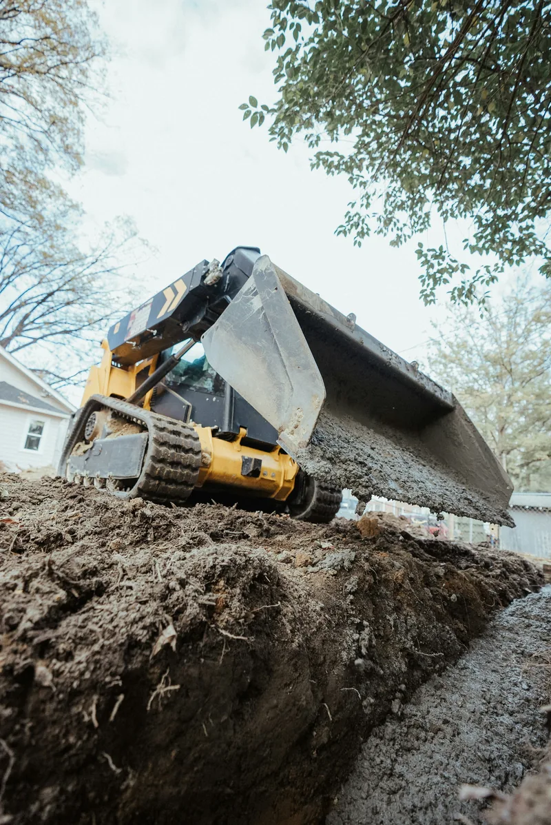 Compact tracked skid steer excavating soil during residential lot clearing near a house in Ontario